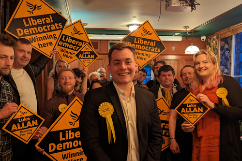2404_Luke_at_CCLE_Launch Luke Allan infront of a group of Lib Dem campaigners holding orange Lib Dem diamonds.