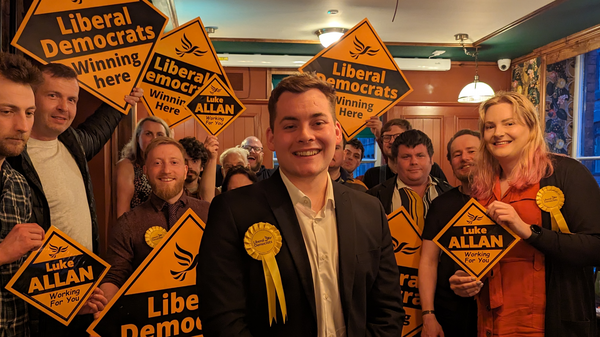Luke Allan infront of a group of Lib Dem campaigners holding orange Lib Dem diamonds.